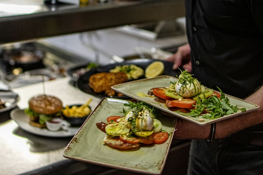 Een ober brengt twee borden met burrata en tomaat naar tafel